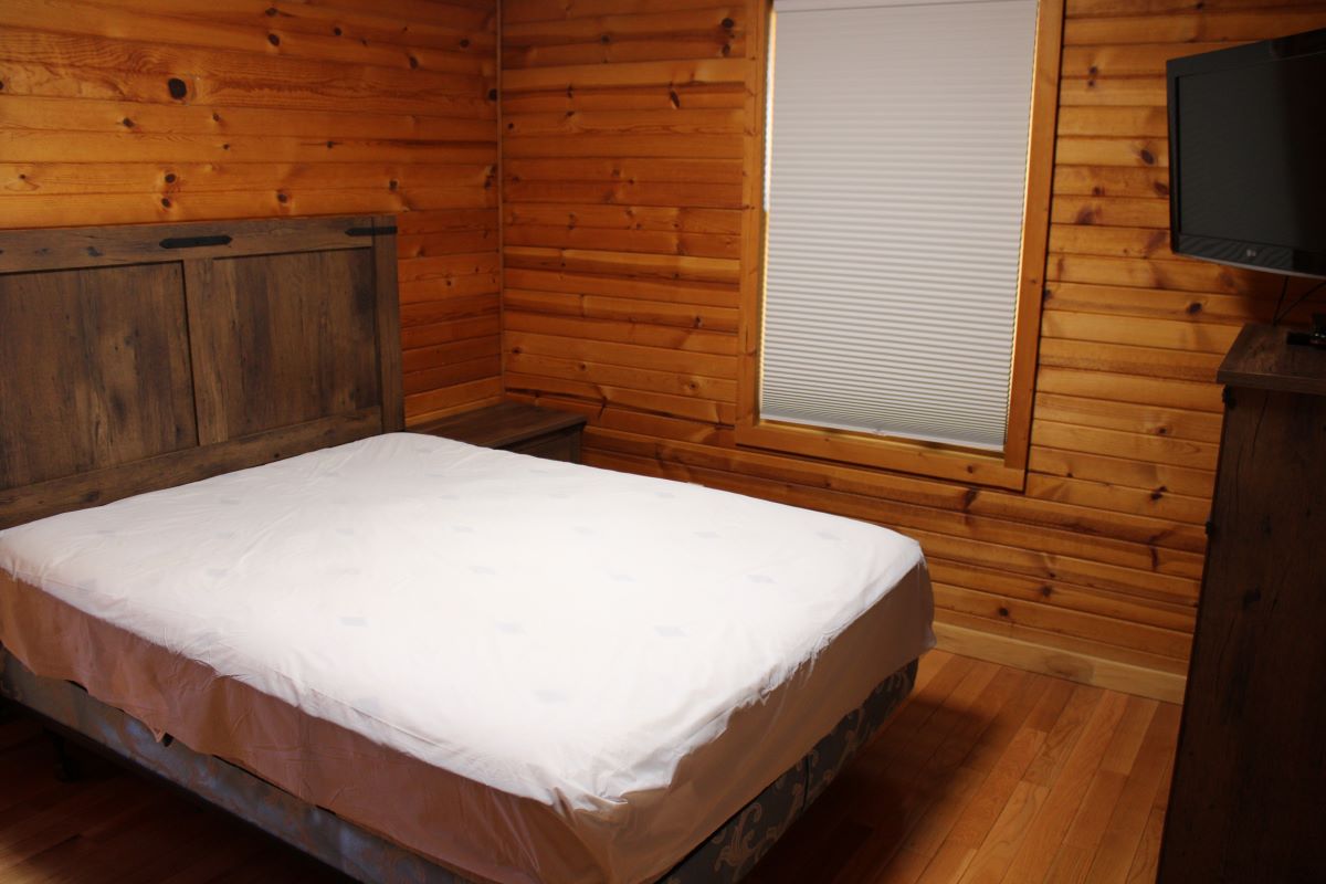 Queen bedroom with dresser and small flatscreen TV in the corner and a window with the shade drawn 