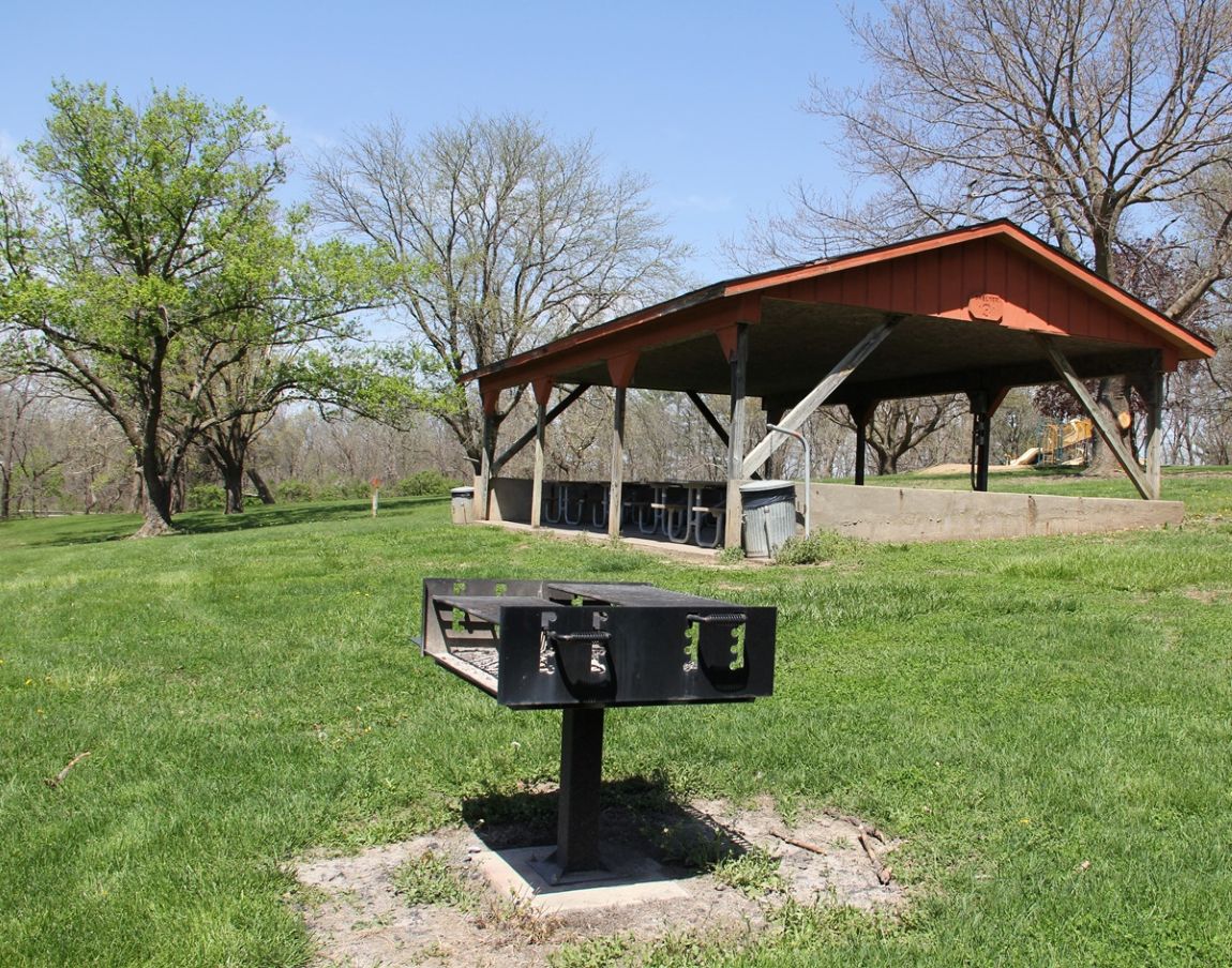 Outdoor shelter house with metal roof, concrete floor, and picnic tables in grassy yard with timber 