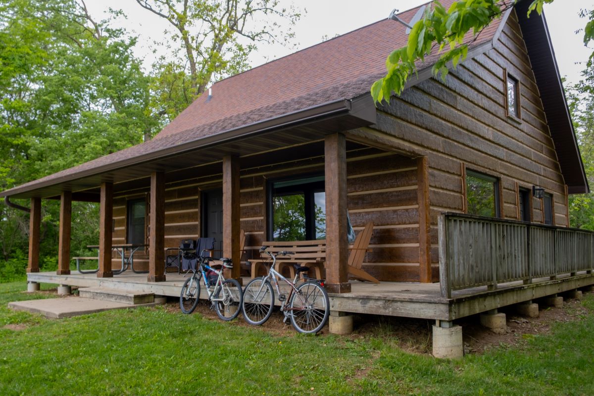 View of the porch on the back on a log style cabin with picnic table, 2 chairs, and a bench. Bikes l