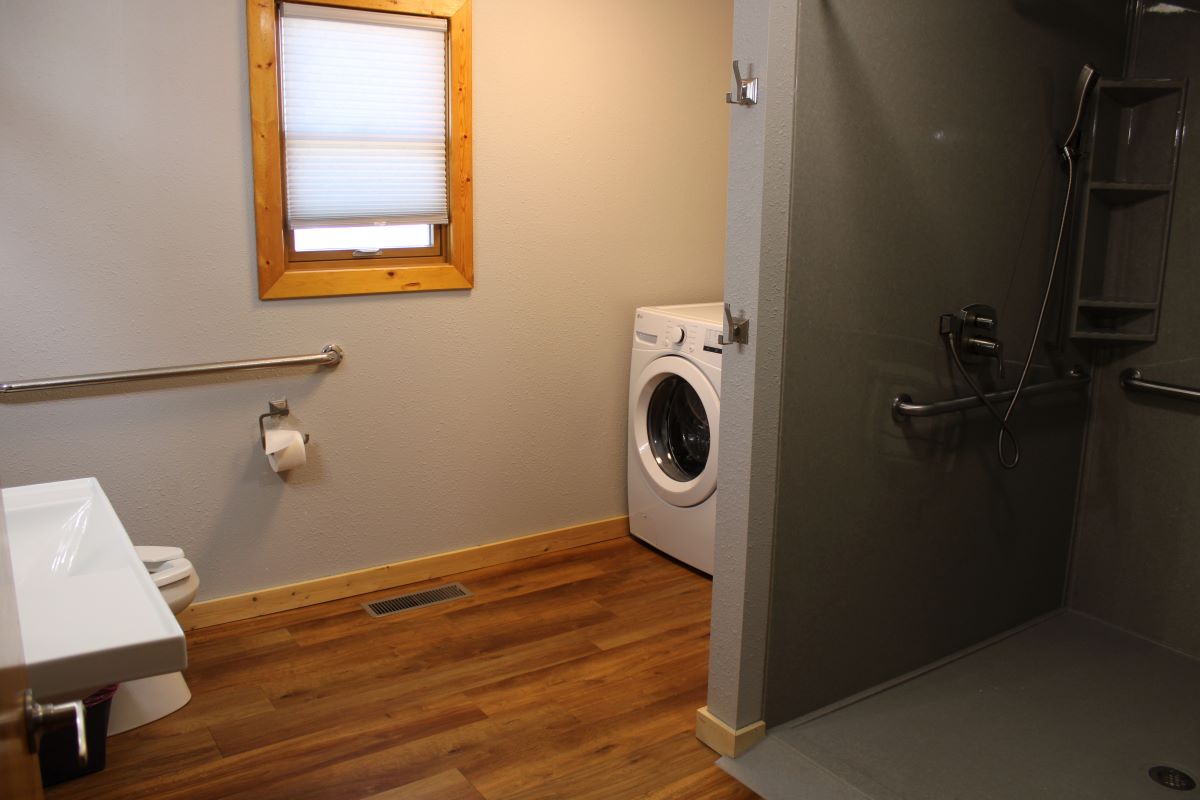 ADA accessible bathroom with walk in shower, vanity sink, grab handles, and laundry area