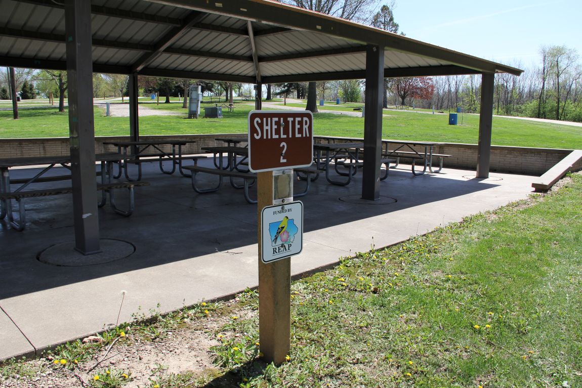 Outdoor shelter house with metal roof, concrete floor, and picnic tables in grassy yard with timber 