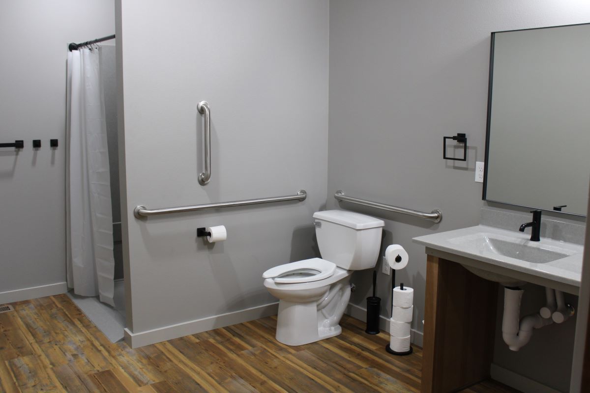 ADA accessible bathroom with toilet, walk in shower, double sink vanity, and large mirror on main fl