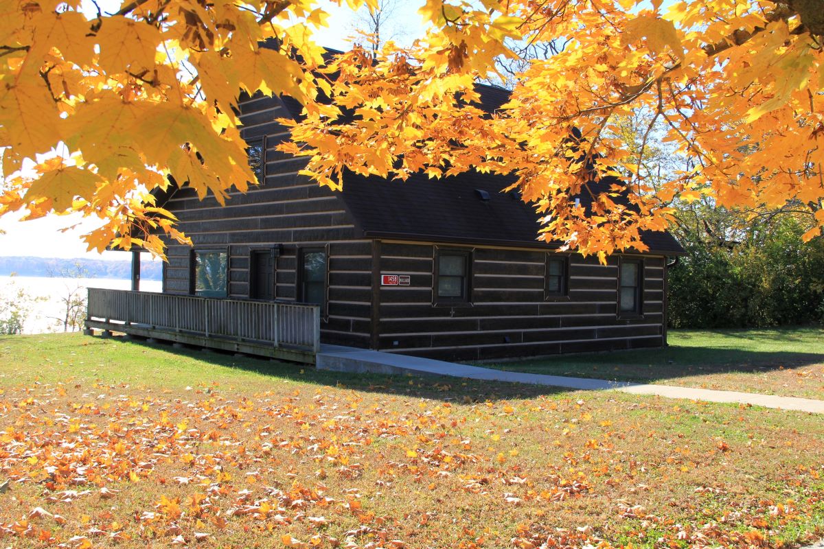 Log style cabin in woods overlooking lake with orange and yellow fall colors with sidewalk leading t