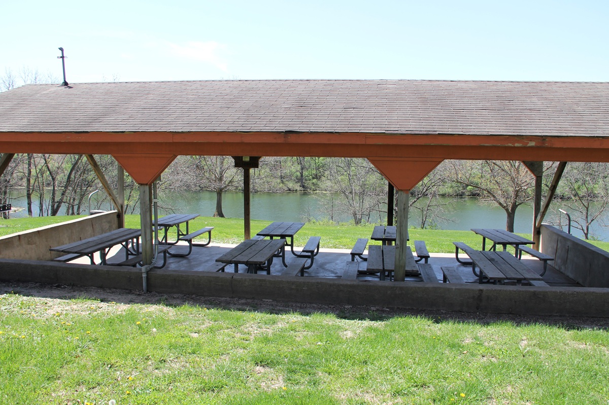 Outdoor shelter house with metal roof, concrete floor, and picnic tables in grassy yard with timber 