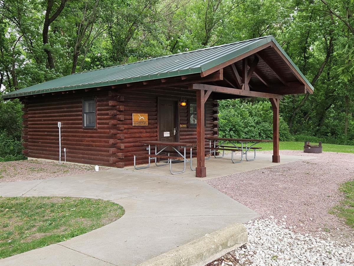 Whitetail - Side view of small log cabin with covered patio, picnic tables and firepit.