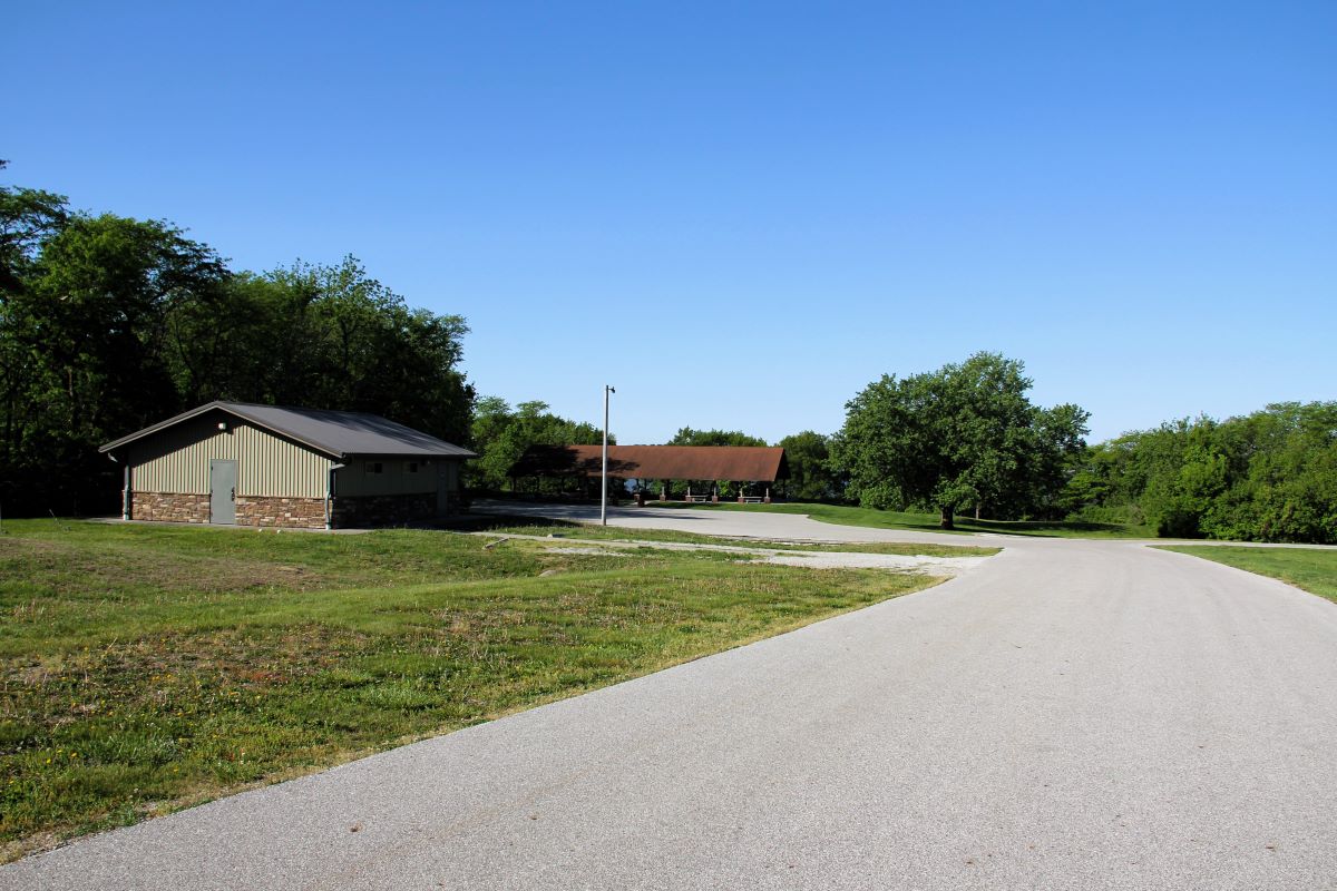 View from the road leading to a large parking lot with a covered outdoor shelter and restroom