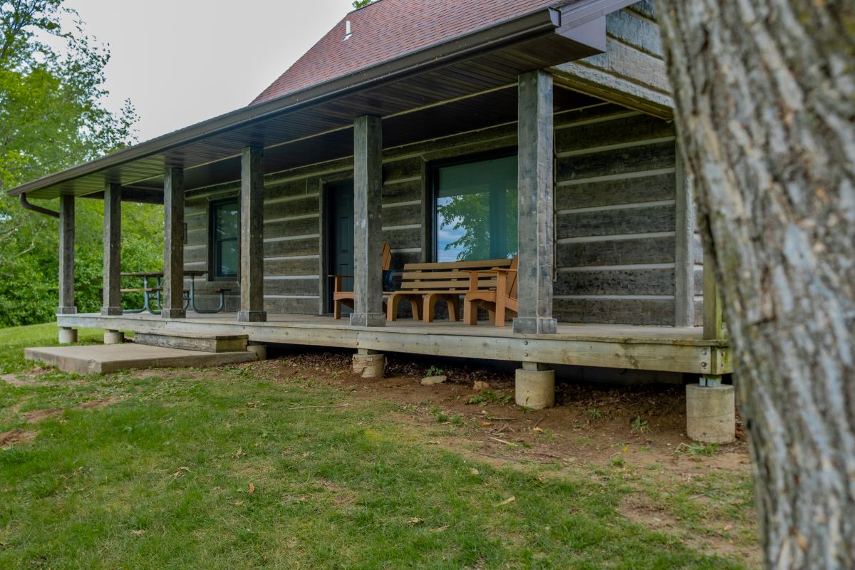 View of the porch on the back on a log style cabin with picnic table, 2 chairs, and a bench