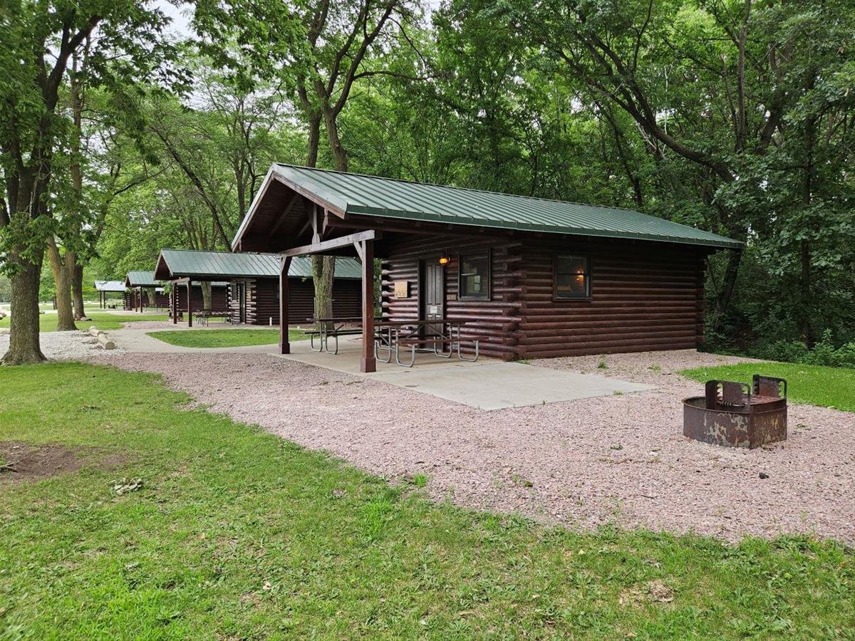 Whitetail - Side view of small log cabin with a covered patio, two picnic tables and firepit.