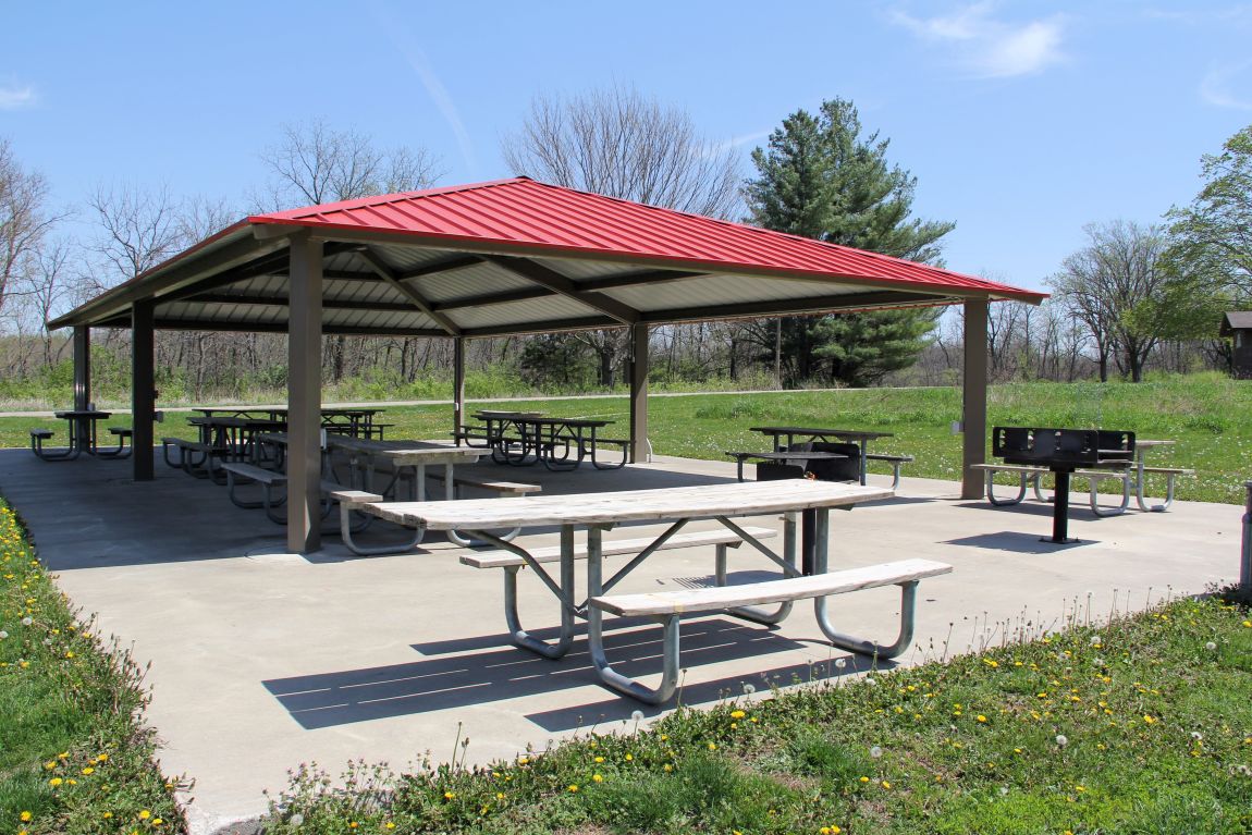 Outdoor shelter house with concrete floor, picnic tables, trash cans, and a metal roof