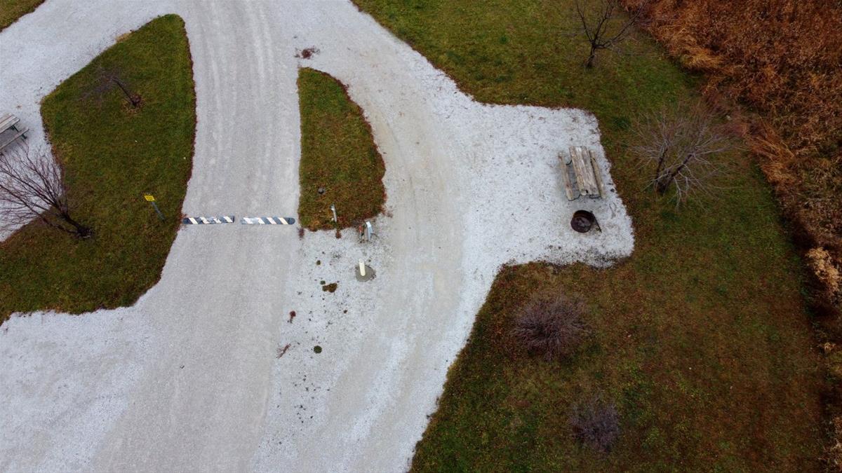 Aerial view of empty camp site with limestone pad, picnic table, fire ring, and trees. 