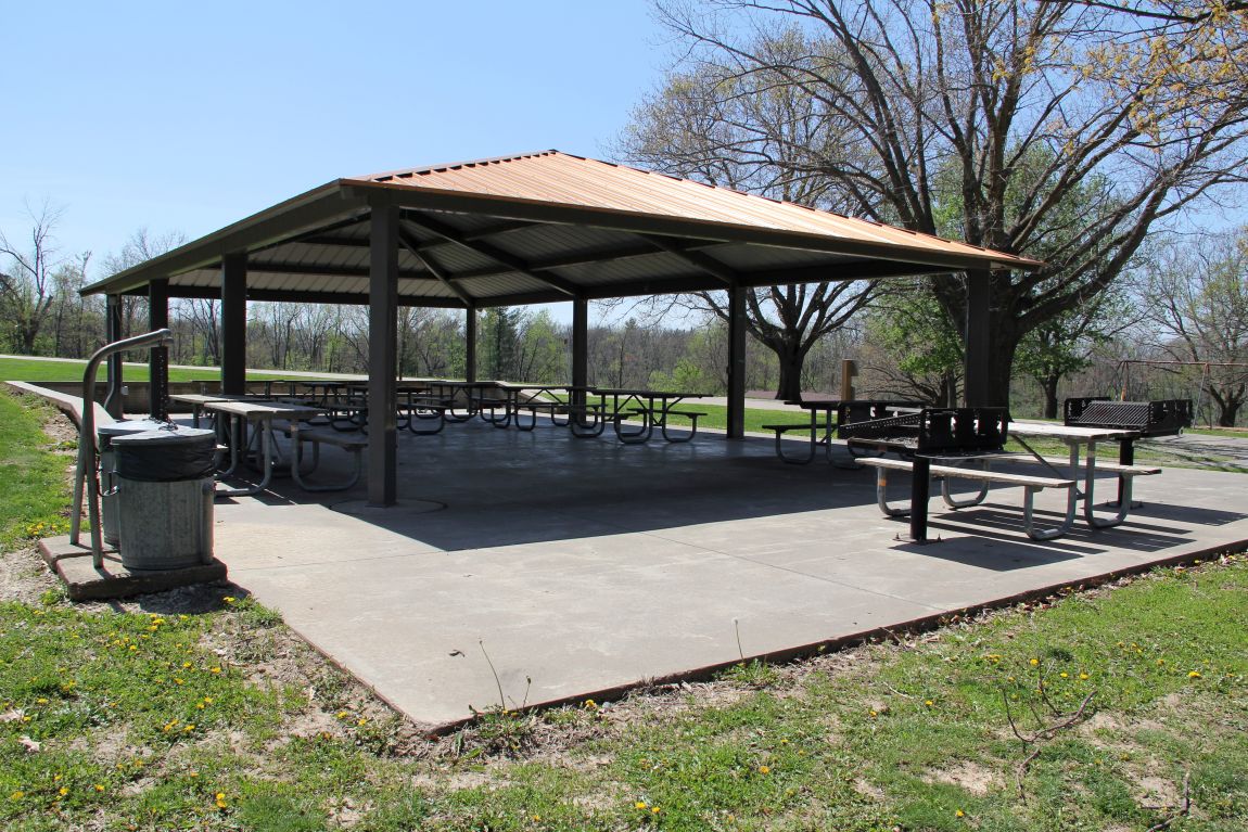 Outdoor shelter house with metal roof, concrete floor, and picnic tables in grassy yard with timber 