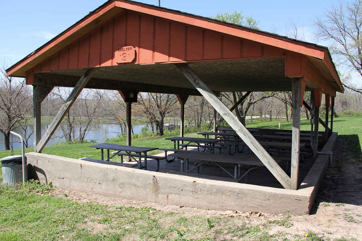 Outdoor shelter house with metal roof, concrete floor, and picnic tables in grassy yard with timber 