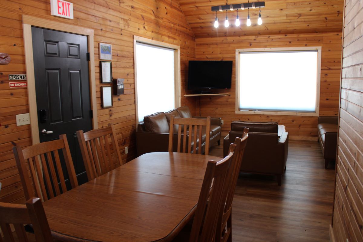 Dining room area overlooking a furnished living room with large windows in a log style cabin