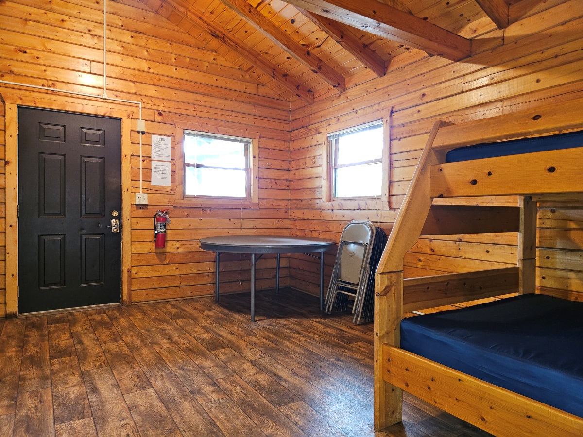Prairie Rose - Cabin interior with wood siding, vinyl plank flooring, folding table & bunkbeds