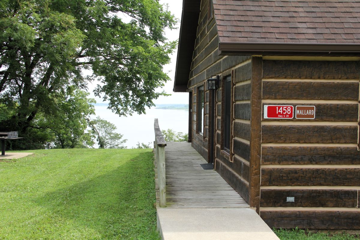 Sidewalk to door and back porch with lake view in the background on log style cabin