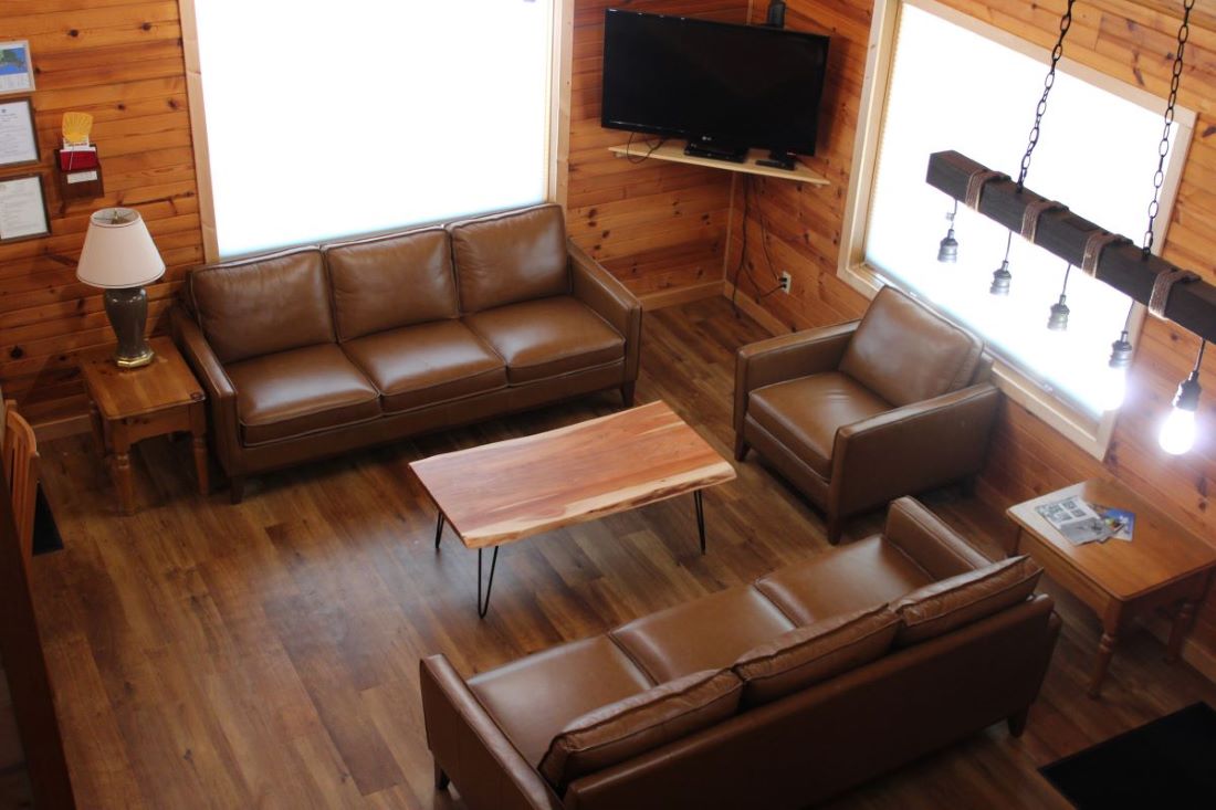 Living room area with sectional, 2 chairs, flat screen TV, and side tables with lamps in log style c