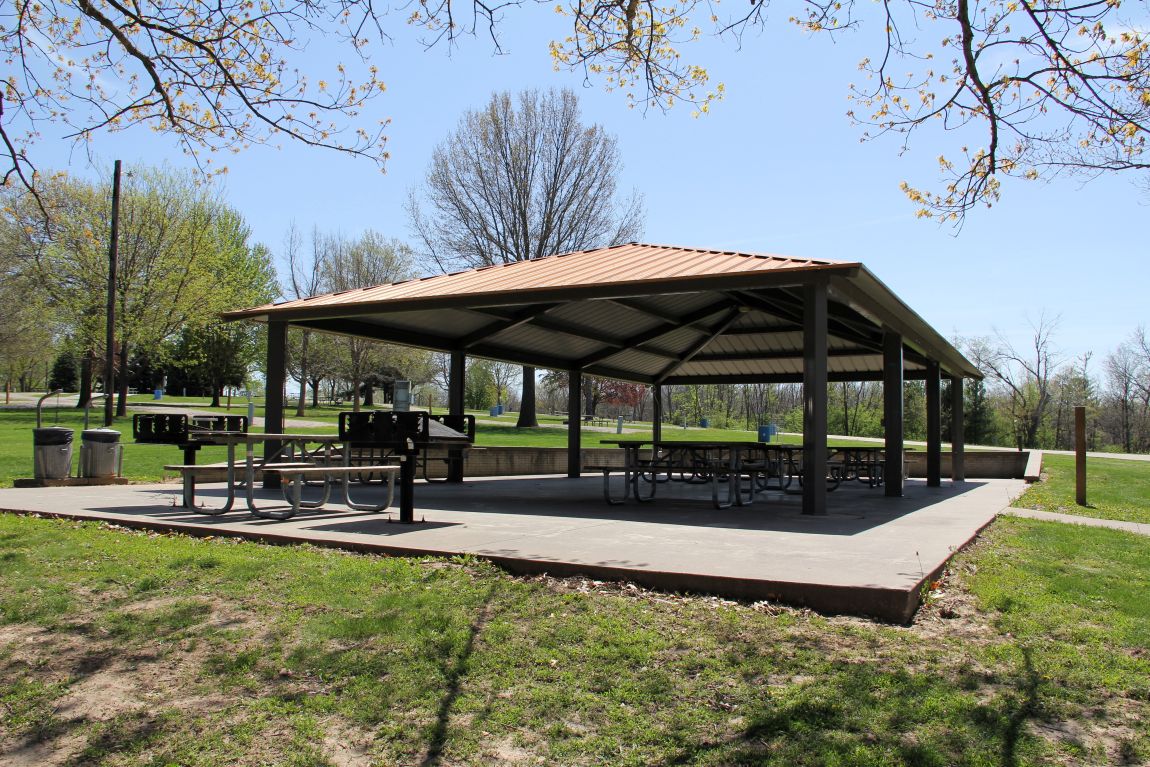 Outdoor shelter house with metal roof, concrete floor, and picnic tables in grassy yard with timber 