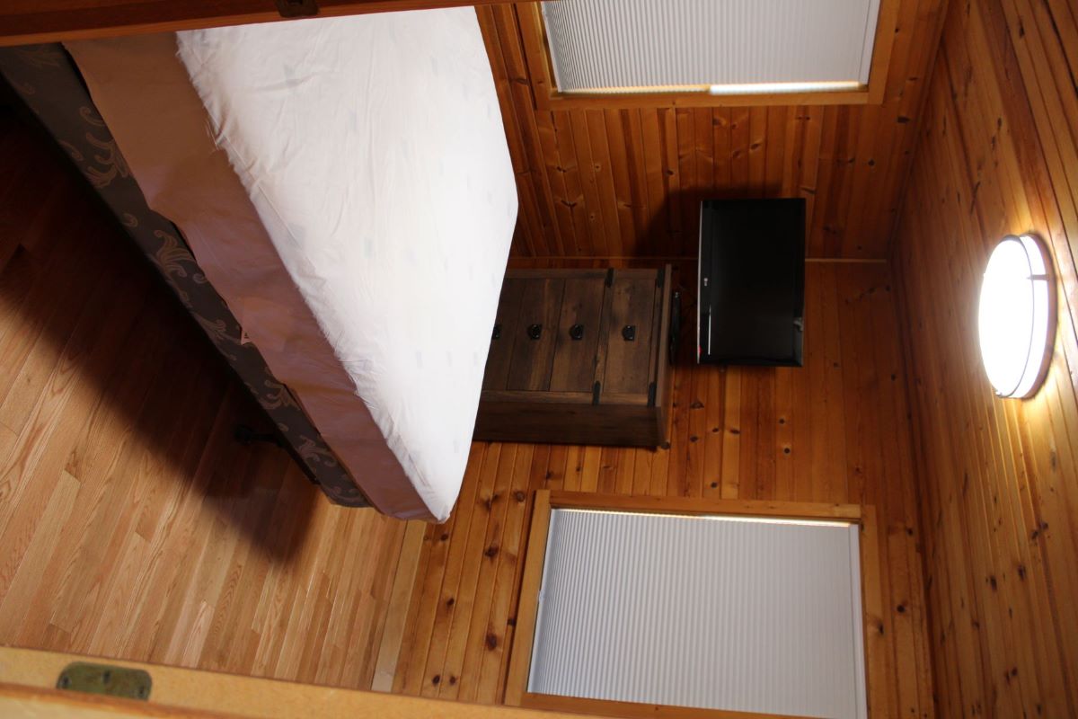 Queen bedroom with dresser and small flatscreen TV in the corner and a window with the shade drawn 