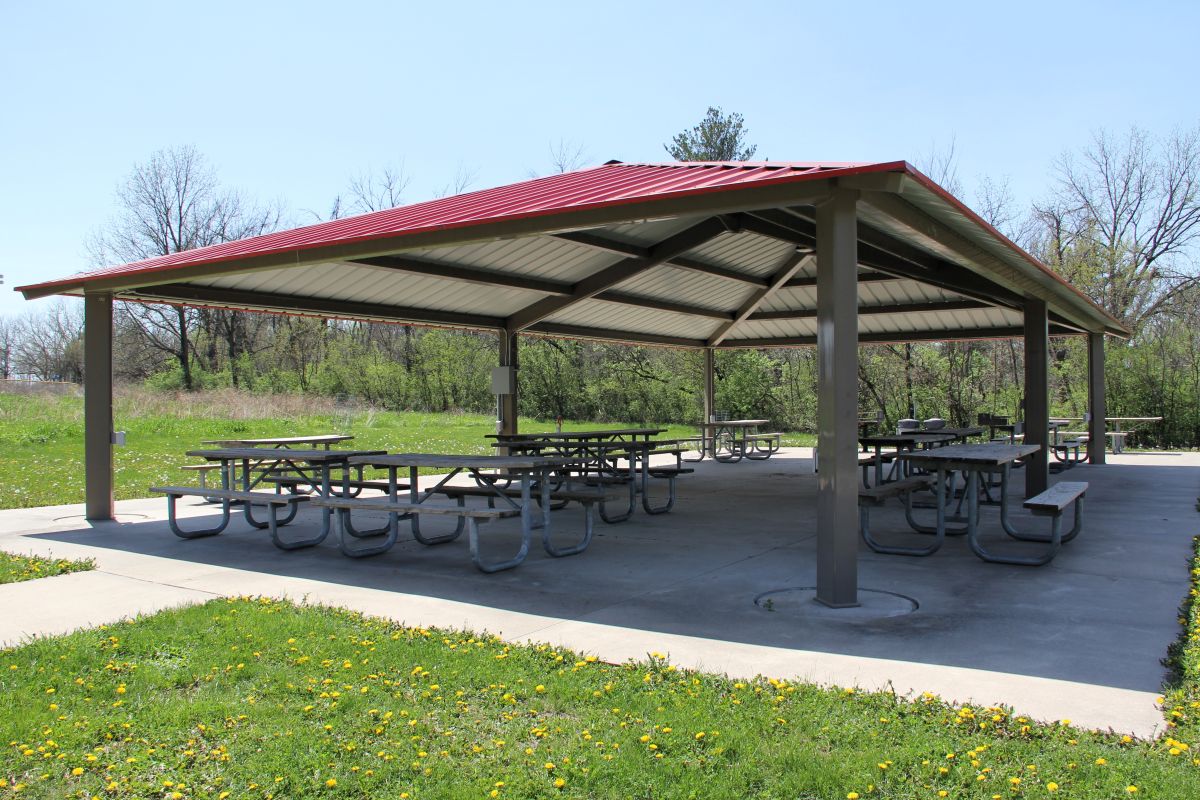 Interior area of outdoor shelter house with concrete floor, picnic tables, trash cans, and a metal r
