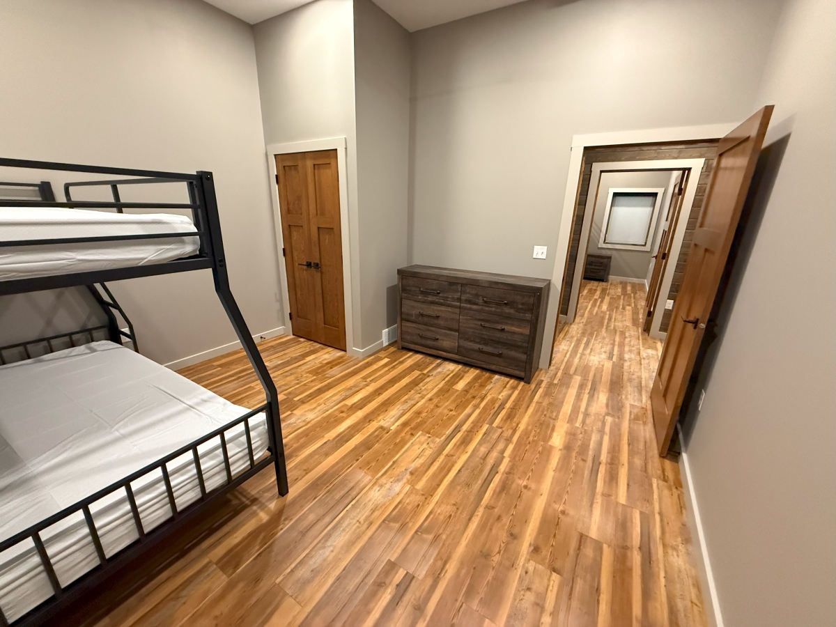 Bunk bedroom in basement with dresser and closet, hallway leading to another bedroom