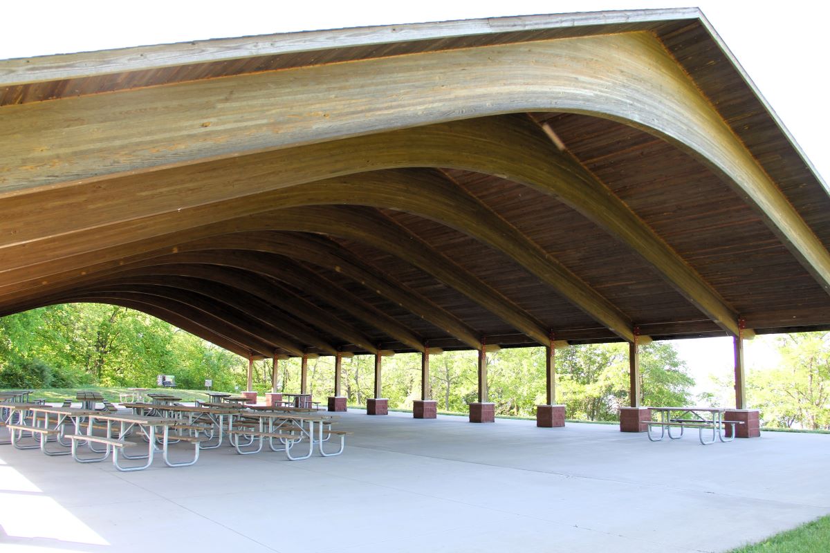 Large open shelter house with arched wood roof and picnic tables on concrete floor