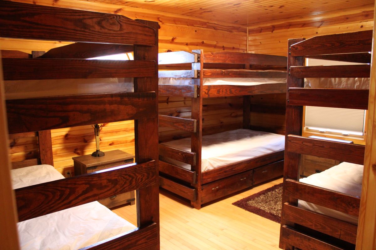 Bunk bedroom with 6 beds total on wood frames with drawers underneath, 2 windows with shades, and 2 