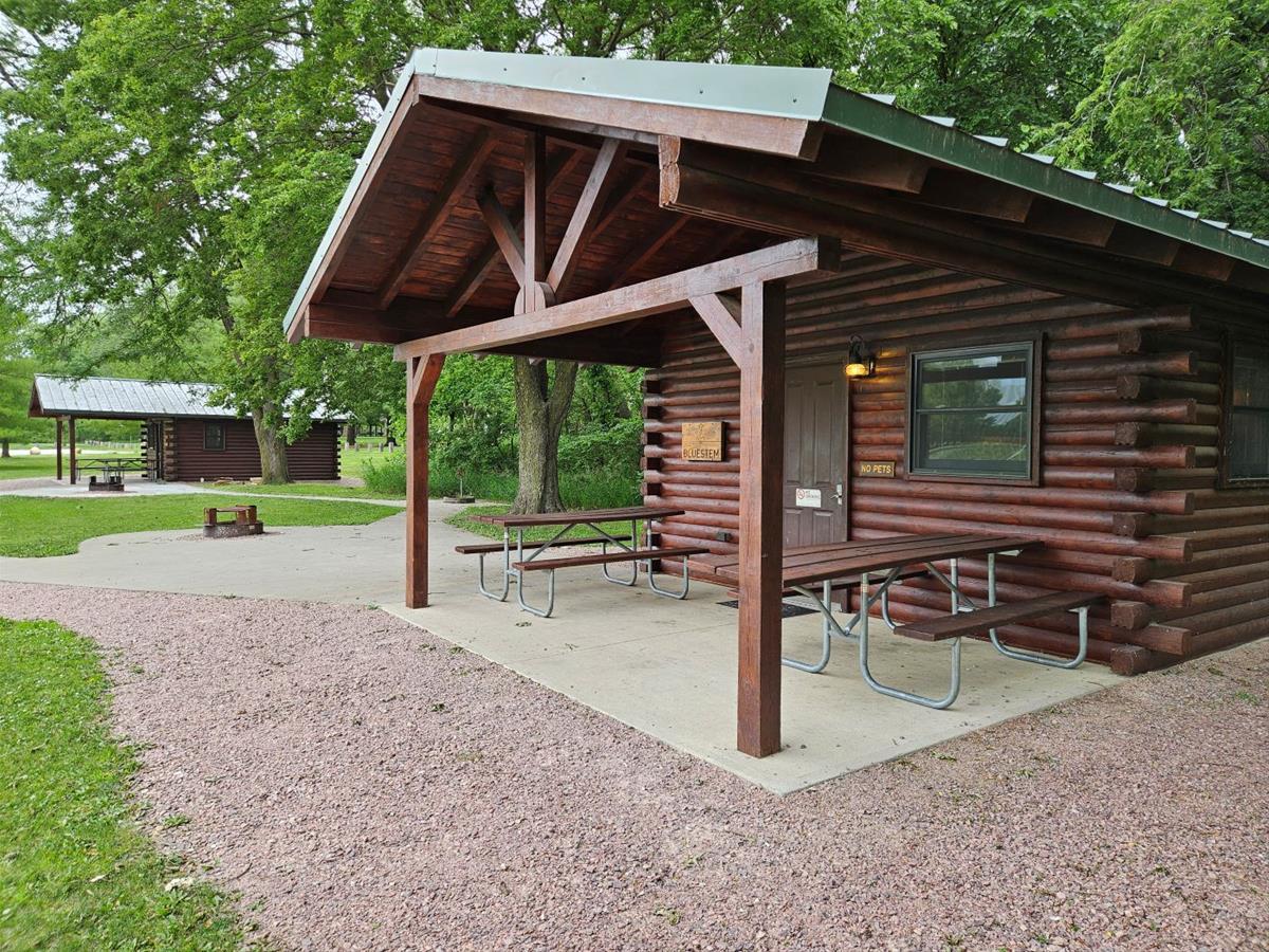 Bluestem - Side view of small log cabin with covered patio, picnic tables and firepit.