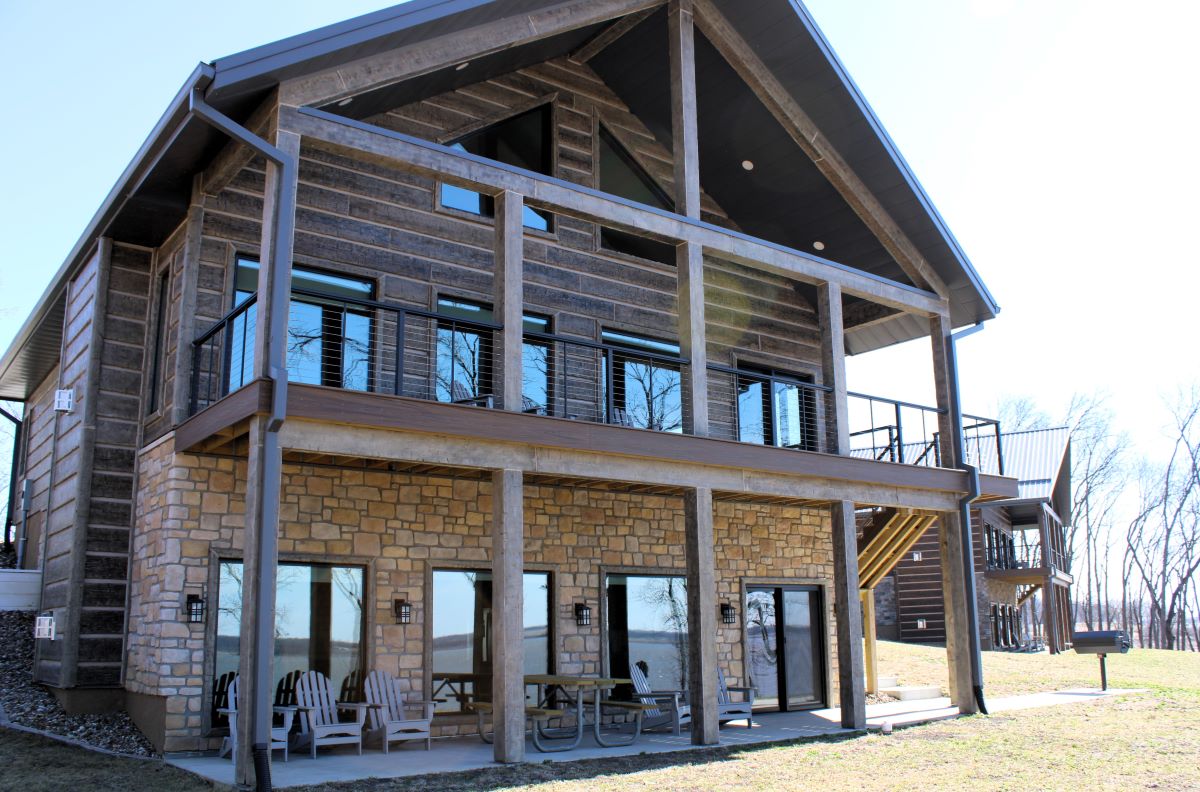 Upper level deck and lower level patio with chairs and picnic table on a modern style cabin, a grill