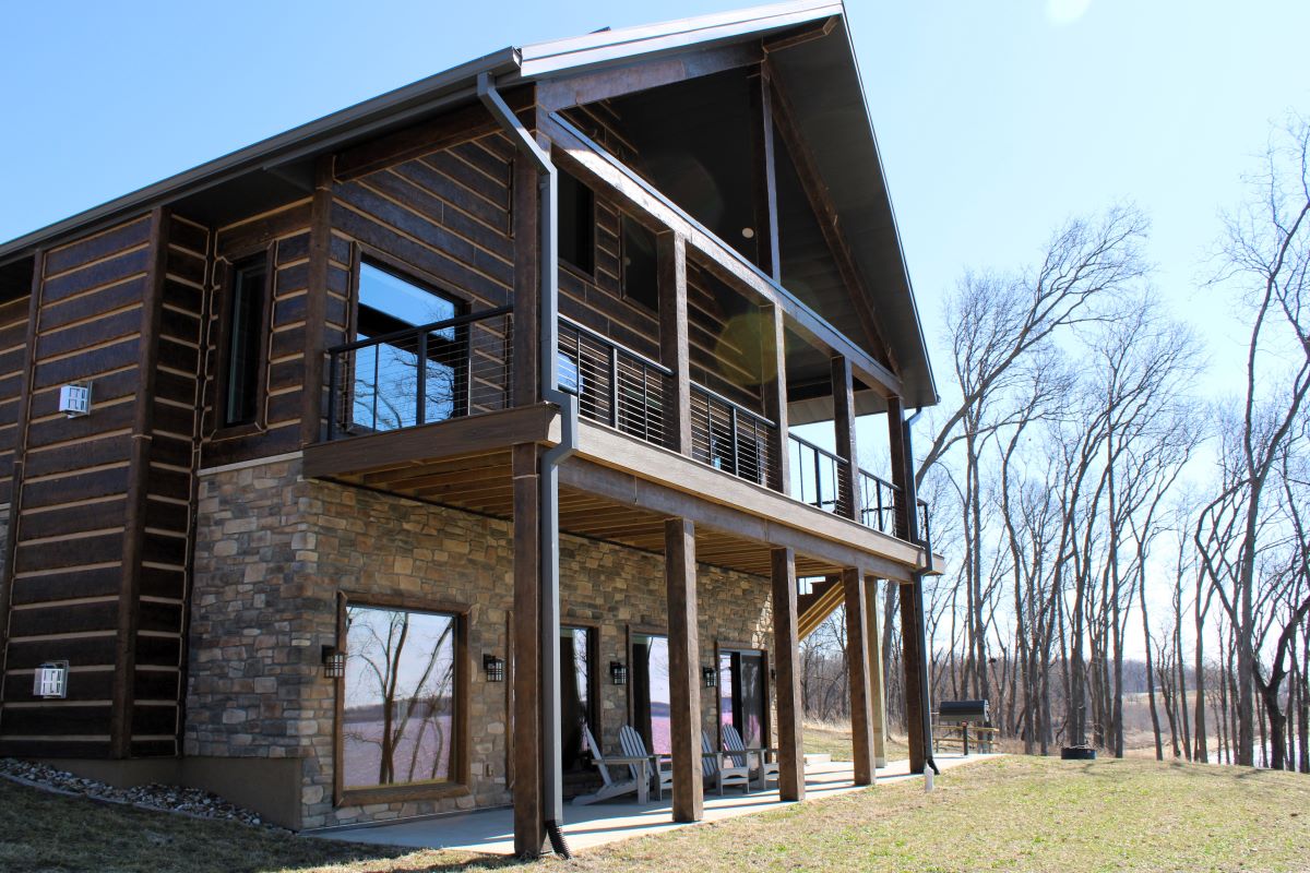Upper level deck and lower level patio with chairs and picnic table on a modern style cabin, a grill