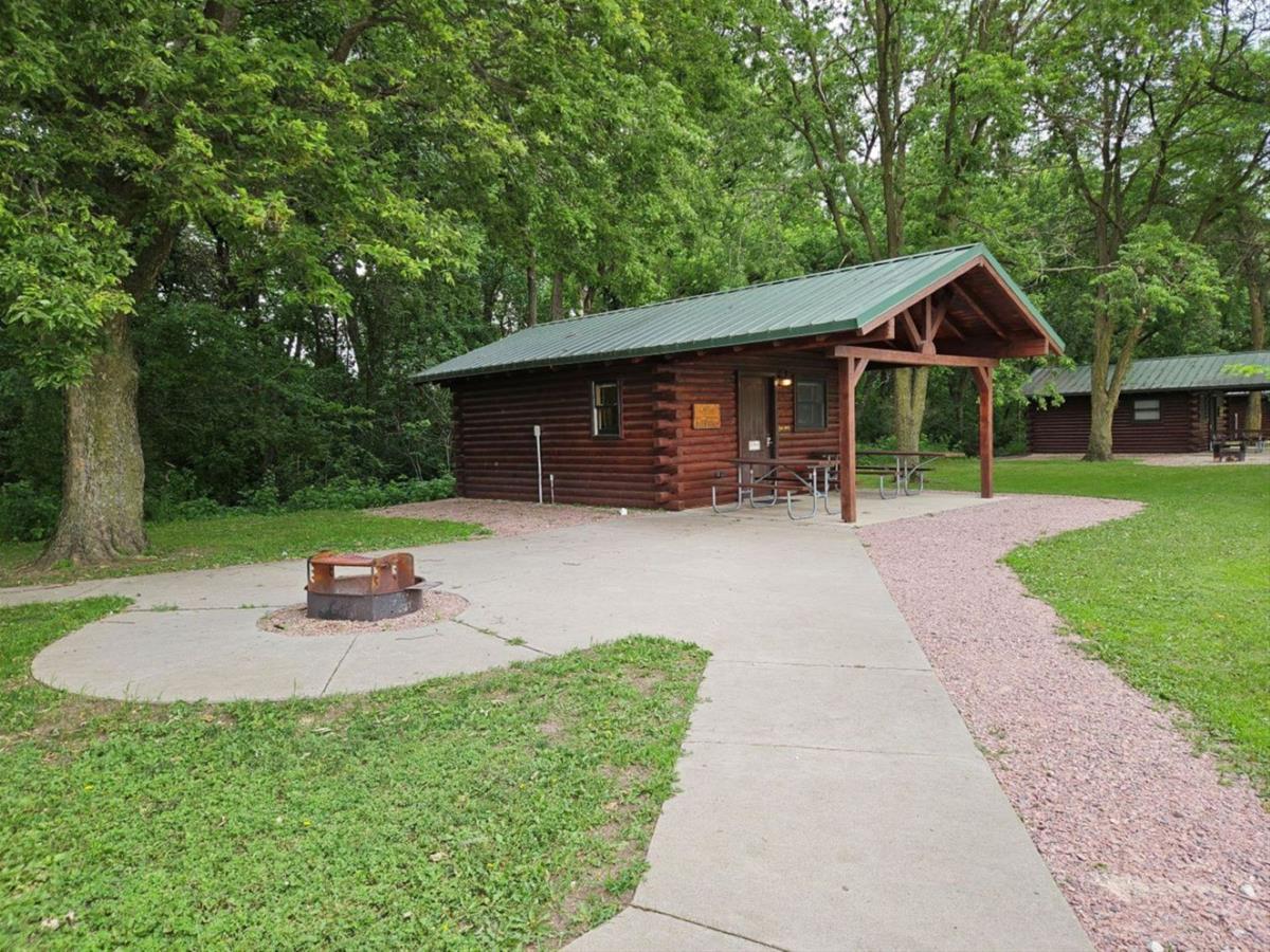 Bluestem - Side view of small log cabin with a covered patio and concrete space with firepit