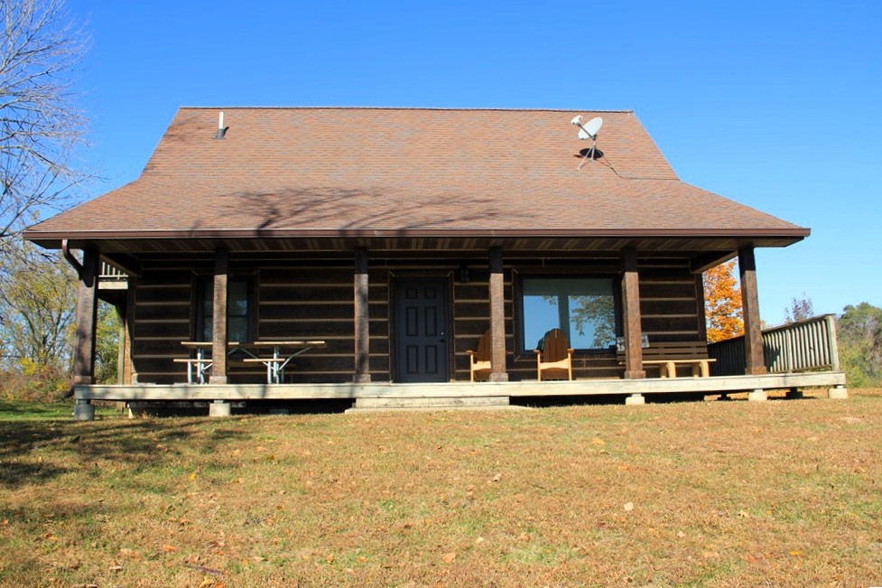 View of the porch on the back of a log style cabin with picnic table, 2 chairs, and a bench 