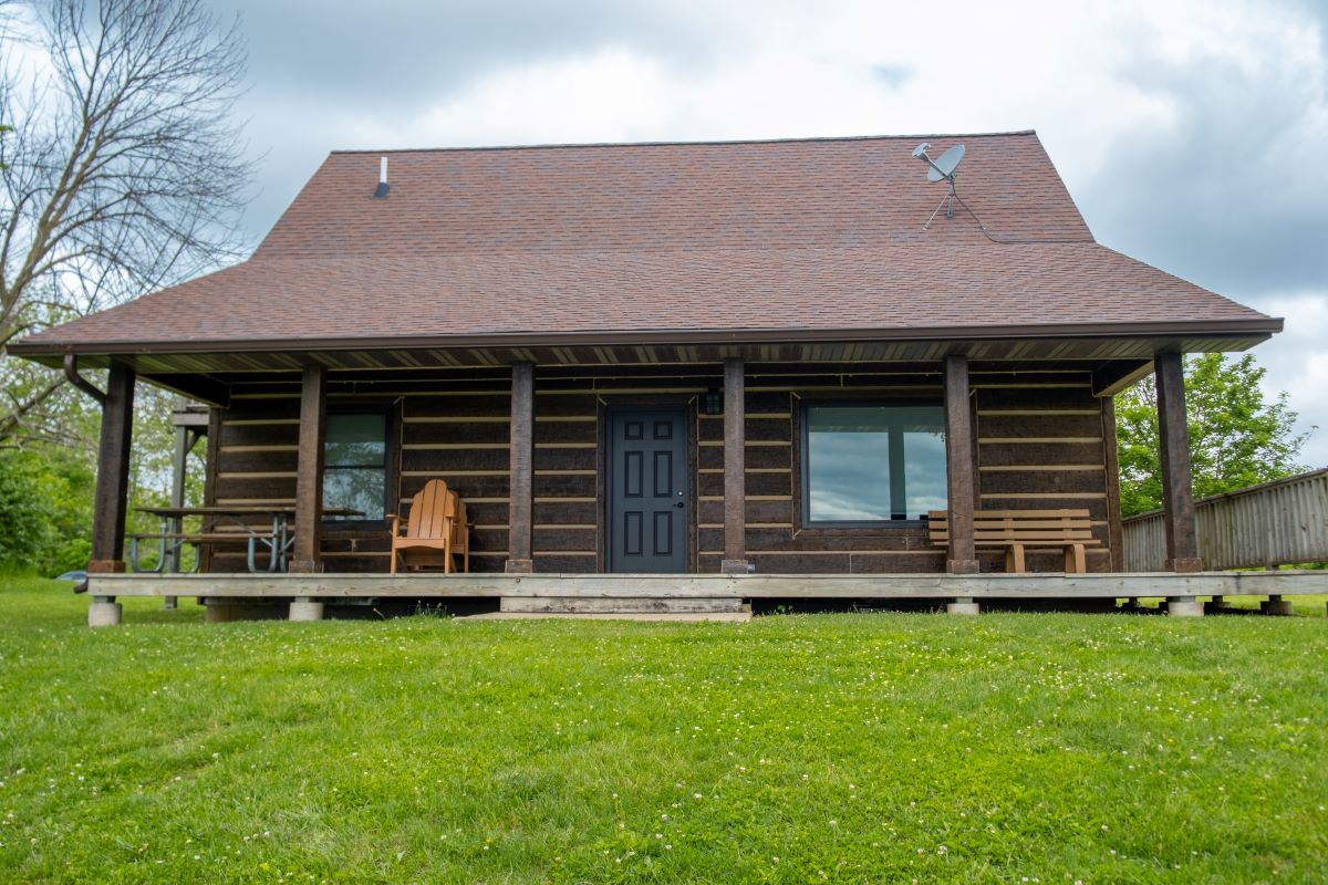 View of the porch on the back on a log style cabin with picnic table, 2 chairs, and a bench summer t