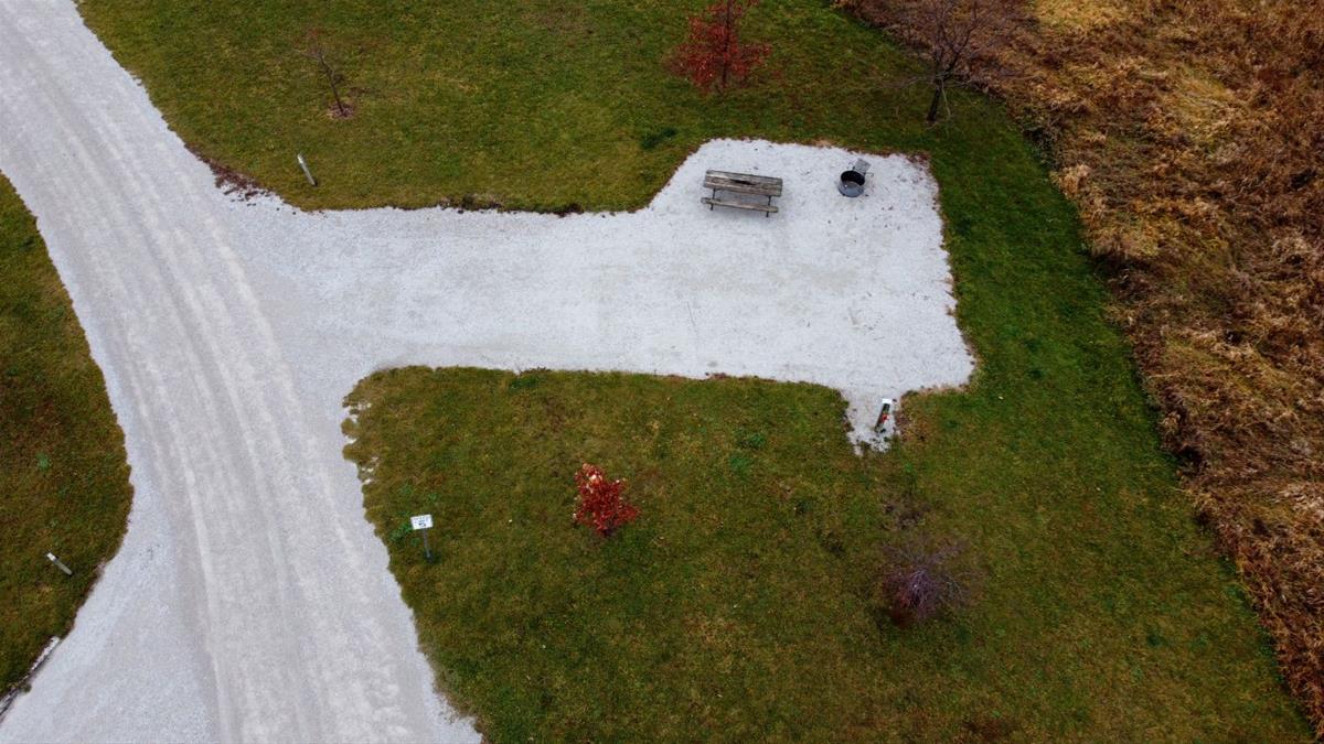 Aerial view of empty camp site with limestone pad, picnic table, fire ring, and trees. 