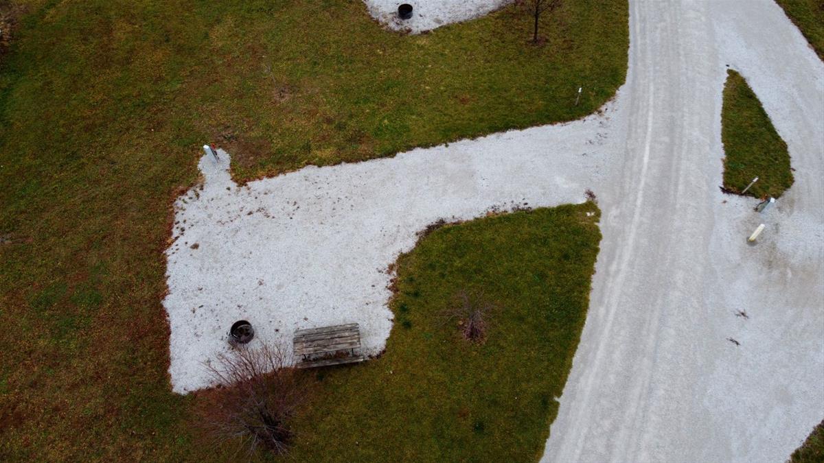 Aerial view of empty camp site with limestone pad, picnic table, fire ring, and trees. 