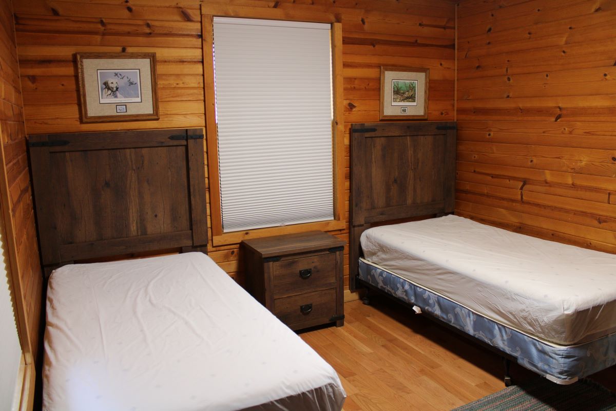 Two twin beds with a nightstand in between and window with the shade drawn