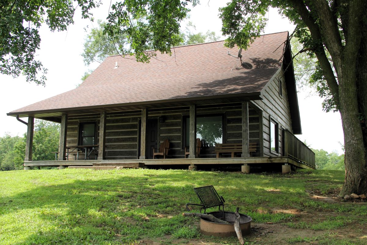 View of the porch on the back on a log style cabin with picnic table, 2 chairs, and a bench