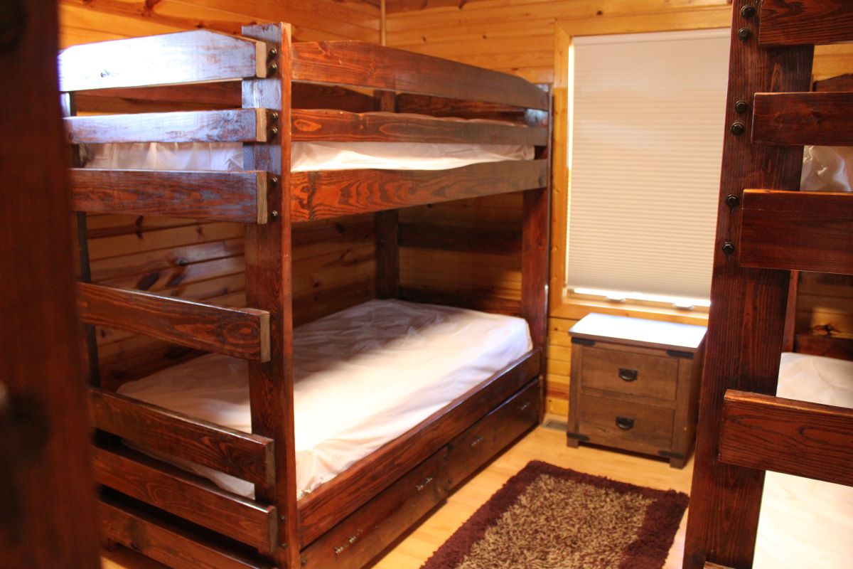 Bunk bedroom with twin beds on wood frames with drawers below and nightstand between them with a win